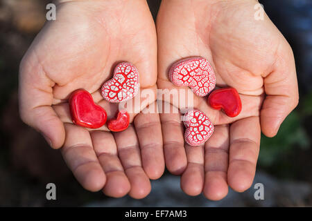 Zwei Hände halten sechs rote-gesprenkelte rote Keramik Herzen. Stockfoto