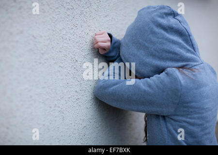 Trauriges Kind in Hoodie mit Gesicht versteckt, lehnte sich gegen eine Wand in Verzweiflung Stockfoto