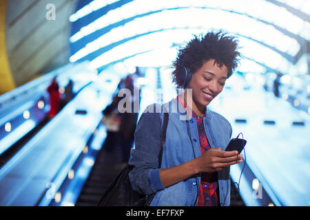 Lächelnde Frau anhören von MP3-Player auf Rolltreppe Stockfoto