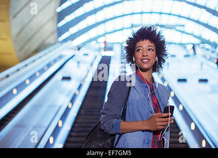 Frau anhören Ohrhörer auf Rolltreppe Stockfoto