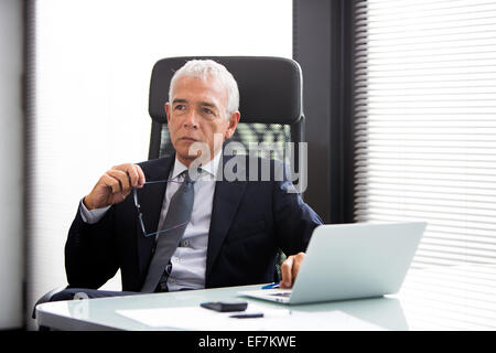 Halblängen Porträt eines durchdachten Geschäftsmann im Büro mit Laptop-Computer und halten Gläser Stockfoto