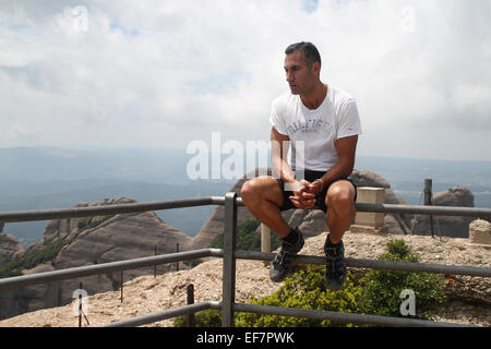 Mann sitzt auf dem Geländer am Aussichtspunkt des Berges Gipfel von Sant Jeroni (1.236 m), Montserrat, Katalonien Stockfoto