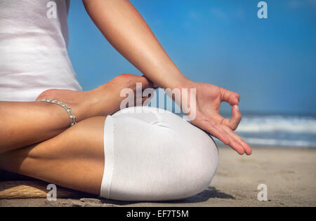 Frau tut Yoga Meditation im weißen Kostüm am Strand von Goa, Indien Stockfoto