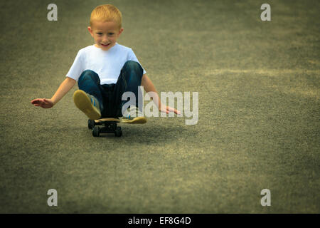 Aktive Kindheit. Kleiner Mann skateboarding. Skater junge Kind sitzt auf Park-Gasse auf Skateboard. Im Freien. Stockfoto