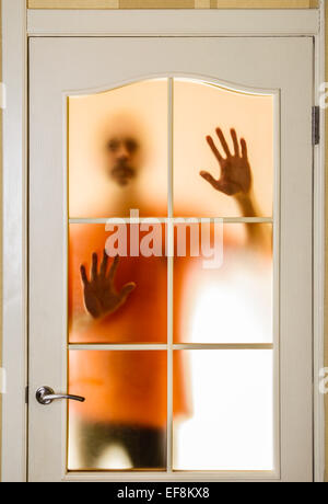 Silhouette von einem unbekannten Mann in Orange gesehen hinter einer verschlossenen Glastür, wie ein Geist oder ein Ausländer Stockfoto