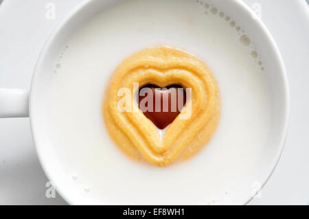 Nahaufnahme einer Tasse mit Milch mit einem herzförmigen Cookie drin Stockfoto