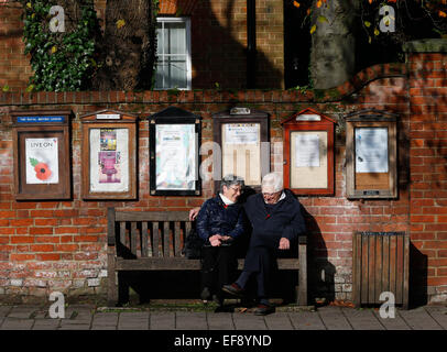 Ein älteres Ehepaar sitzen auf einer Bank zu einem Gespräch unter schwarzen Brettern in Hartley Wintney, Haken November 2014 haben Stockfoto