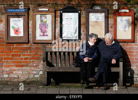 Ein älteres Ehepaar sitzen auf einer Bank zu einem Gespräch unter schwarzen Brettern in Hartley Wintney, Haken November 2014 haben Stockfoto