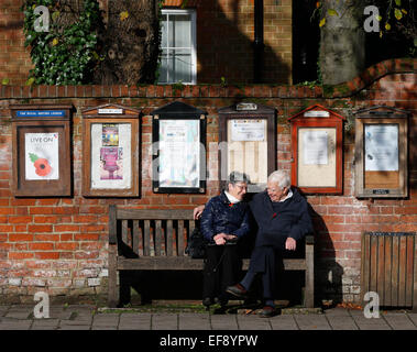 Ein älteres Ehepaar sitzen auf einer Bank zu einem Gespräch unter schwarzen Brettern in Hartley Wintney, Haken November 2014 haben Stockfoto