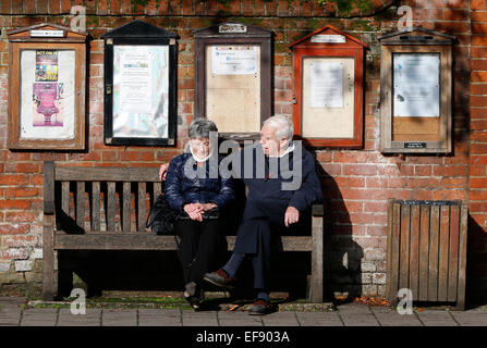 Ein älteres Ehepaar sitzen auf einer Bank zu einem Gespräch unter schwarzen Brettern in Hartley Wintney, Haken November 2014 haben Stockfoto