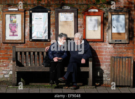 Ein älteres Ehepaar sitzen auf einer Bank zu einem Gespräch unter schwarzen Brettern in Hartley Wintney, Haken November 2014 haben Stockfoto