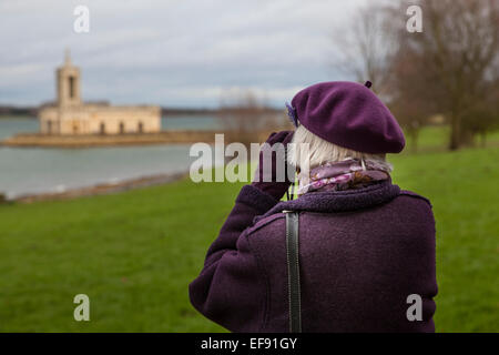 Ältere Frau trägt einen lila Mütze und Mantel und schauen durch ein Fernglas in Normanton Church Rutland Water. Stockfoto