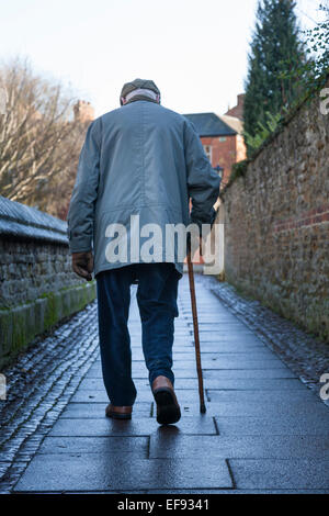 Ein älterer Mann mit einem Gehstock Spaziergänge auf dem feuchten Weg der Pflastersteine zwischen zwei Steinmauern in Oakham, Rutland. Stockfoto