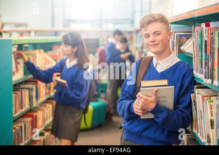 Porträt von lächelnden männlichen Studenten tragen blaue Schule einheitliche halten Bücher in der Bibliothek Stockfoto