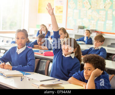 Grundschulkinder im Klassenzimmer während der Lektion, lächelndes Mädchen Hand heben Stockfoto