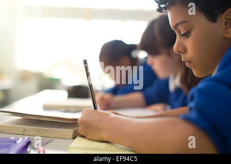 Schülerinnen und Schüler schreiben in Notebooks am Schreibtisch im Klassenzimmer Stockfoto