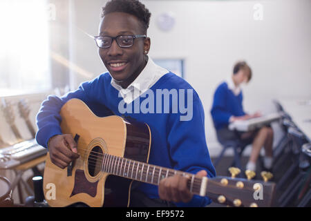 Porträt von lächelnden männlichen Studenten spielt akustische Gitarre im Klassenzimmer Stockfoto