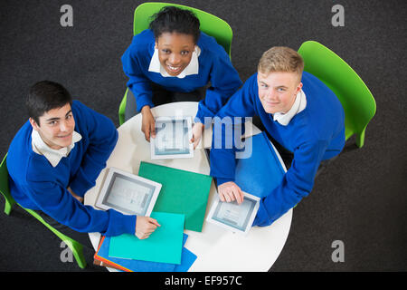 Obenliegende Porträt von drei Studenten mit digitalen Brettchen am runden Tisch zusammen sitzen Stockfoto