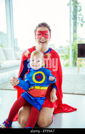 Superheld umarmt Tochter am Boden des Wohnzimmers Stockfoto