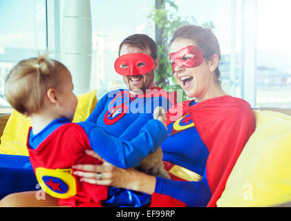 Superhelden-Eltern spielen mit Tochter auf dem Sofa im Wohnzimmer Stockfoto