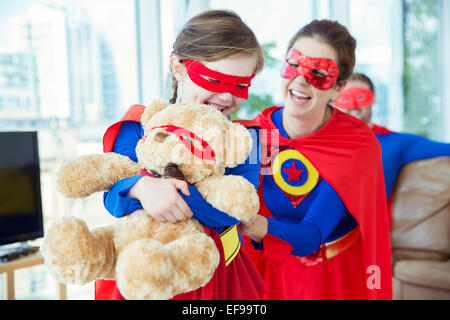 Superhelden-Mutter und Tochter spielen mit Teddybär Stockfoto