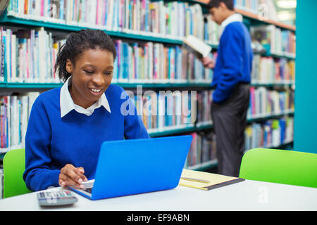 Lächelnde Studentin mit Laptop in der Bibliothek Stockfoto