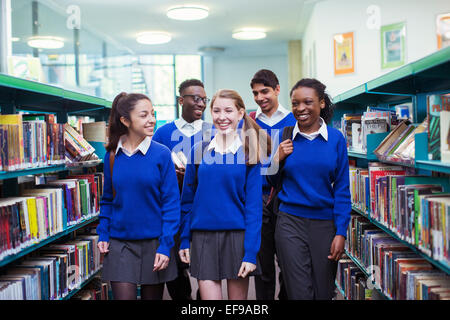 Lächelnde Studenten tragen blaue Schuluniformen zu Fuß zwischen den Bücherregalen in Bibliothek Stockfoto