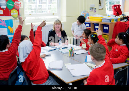 Frage in der Klasse am Londoner Grundschule Lehrer. Engagierte Kinder heben ihre Hände mit der Antwort Stockfoto