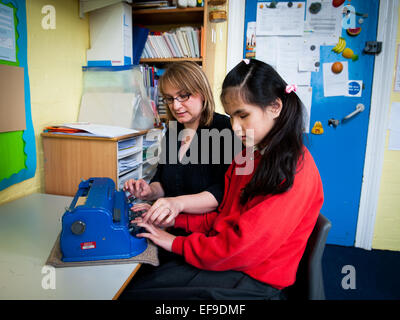 Blindes Mädchen mit Lehrer und Braille-Schreibmaschine in Special Needs-Klasse in London Grundschule Stockfoto