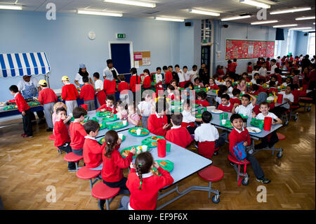 Schulabendessen - Mittagszeit in der britischen State Primary School Lehrer und Grundschulkinder in der Primary School Stockfoto