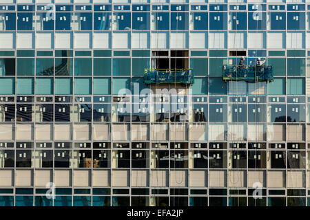 Arbeiter inspizieren die Fenster eines Gebäudes, das gerade renoviert wird. Das Yoyogi National Gymnasium spiegelt sich in den Fenstern wider. Tokio, Japan Stockfoto