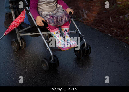 Ein Kleinkind Mädchen reiten in einem Kinderwagen an einem regnerischen Tag. Stockfoto