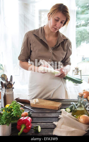 Frau reinigt den Lauch auf Holztisch in der Nähe von Fenster. Rustikalen Stil. Stockfoto