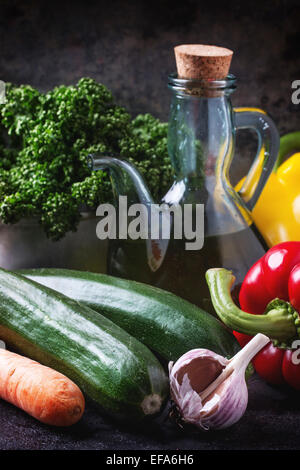 Gemüse und Petersilie mit Olivenöl in Glasflasche auf dunklem Hintergrund Stockfoto