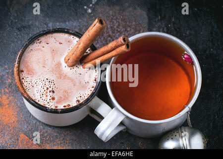 Zwei Vintage Tassen mit Tee und heiße Schokolade mit trockenen Tee serviert, Rosenknospen, gehackte Schokolade und Zimt-sticks über schwarze ba Stockfoto