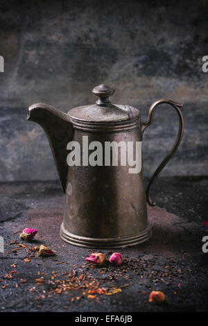 Vintage Teekanne mit trockenen Tee und Rosenknospen über schwarzen Metall Hintergrund Stockfoto