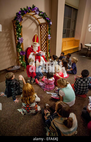 Verkleidet als St. Nikolaus, Freiwilliger in der katholischen Kirche St. Timothy liest Laguna Niguel, CA, Weihnachtsgeschichten multirassische Gemeindemitglied Kinder im Advent, die Zeit der Vorbereitung auf die Feier der Geburt Jesu zu Weihnachten symbolisiert. Stockfoto