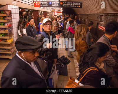 Gemischtrassig Passagiere warten auf einen Zug auf einer u-Bahn-Bahnsteig in New York City. Beachten Sie die Beschilderung. Stockfoto