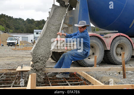 Ein Baumeister leitet Frischbeton aus einem Zement-LKW in das Fundament eines großen Gebäudes. Stockfoto