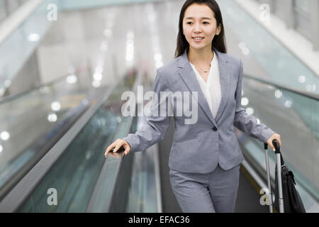 Junge Geschäftsfrau mit Koffer auf Rolltreppe Stockfoto