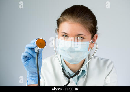 junge Ärztin trägt Latex-Handschuhen und Maske und hält ein Stethoskop Stockfoto