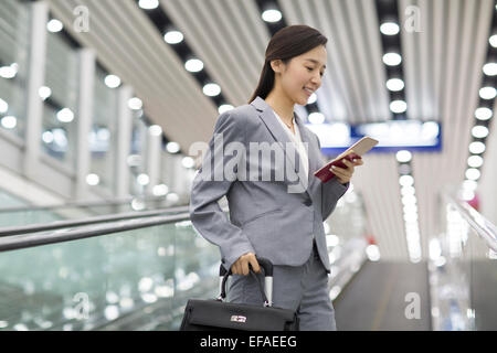 Junge Geschäftsfrau mit Smartphone auf Rolltreppe Stockfoto