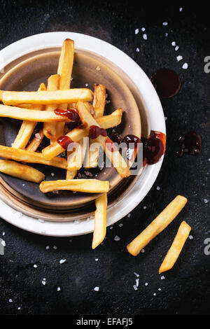 Keramik Teller mit Pommes Frites mit Meersalz und Ketchup auf schwarzem Hintergrund, Ansicht von oben Stockfoto