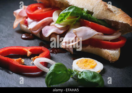 Sandwich mit Schinken, Eiern, Gemüse und Ketchup auf schwarzem Hintergrund. Serien ansehen Stockfoto
