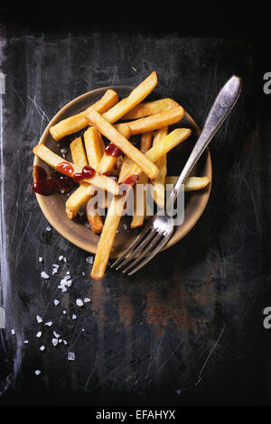 Keramik Teller mit Pommes Frites mit Meersalz und Ketchup, serviert mit Vintage Gabel auf schwarzem Hintergrund, Ansicht von oben Stockfoto