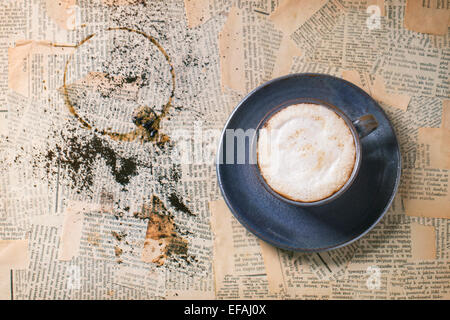 Blaue Keramik Tasse Cappuccino über alte Zeitung. Ansicht von oben. Stockfoto