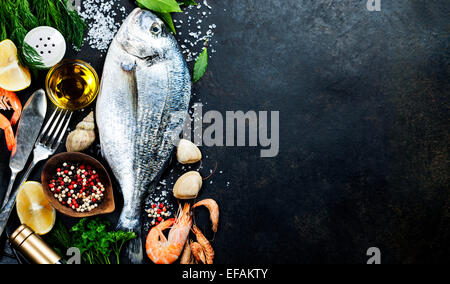 Köstlichen frischen Fisch auf dunkle Vintage-Hintergrund. Fisch mit aromatischen Kräutern, Gewürzen und Gemüse - gesunde Ernährung, Diät oder Kochen Stockfoto