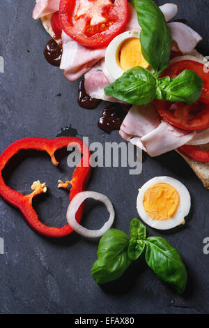 Sandwich mit Schinken, Eiern, Gemüse und Ketchup auf schwarzem Hintergrund. Ansicht von oben Stockfoto