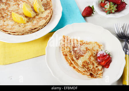 Laskiaispulla Pancake Pfannkuchen Dienstag mit Zitronen und Erdbeeren mit gelben und blauen Servietten auf weiße Vintage shabby chic Tisch. Stockfoto