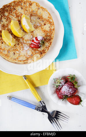 Laskiaispulla Pancake Pfannkuchen Dienstag mit Zitronen und Erdbeeren mit gelben und blauen Servietten auf weiße Vintage shabby chic Tisch. Stockfoto